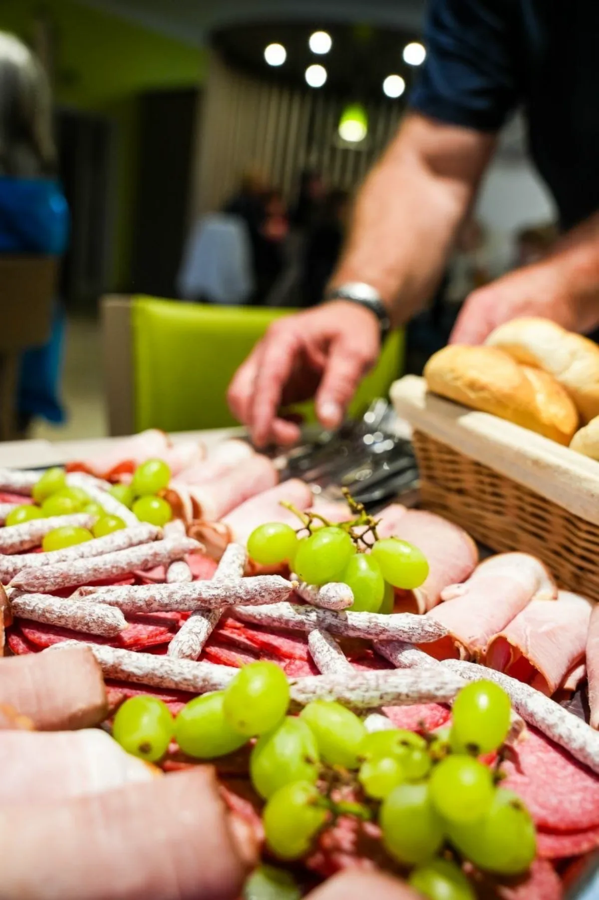 Brotzeitplatte mit Schinken, Wurst und Trauben wird am Tisch serviert