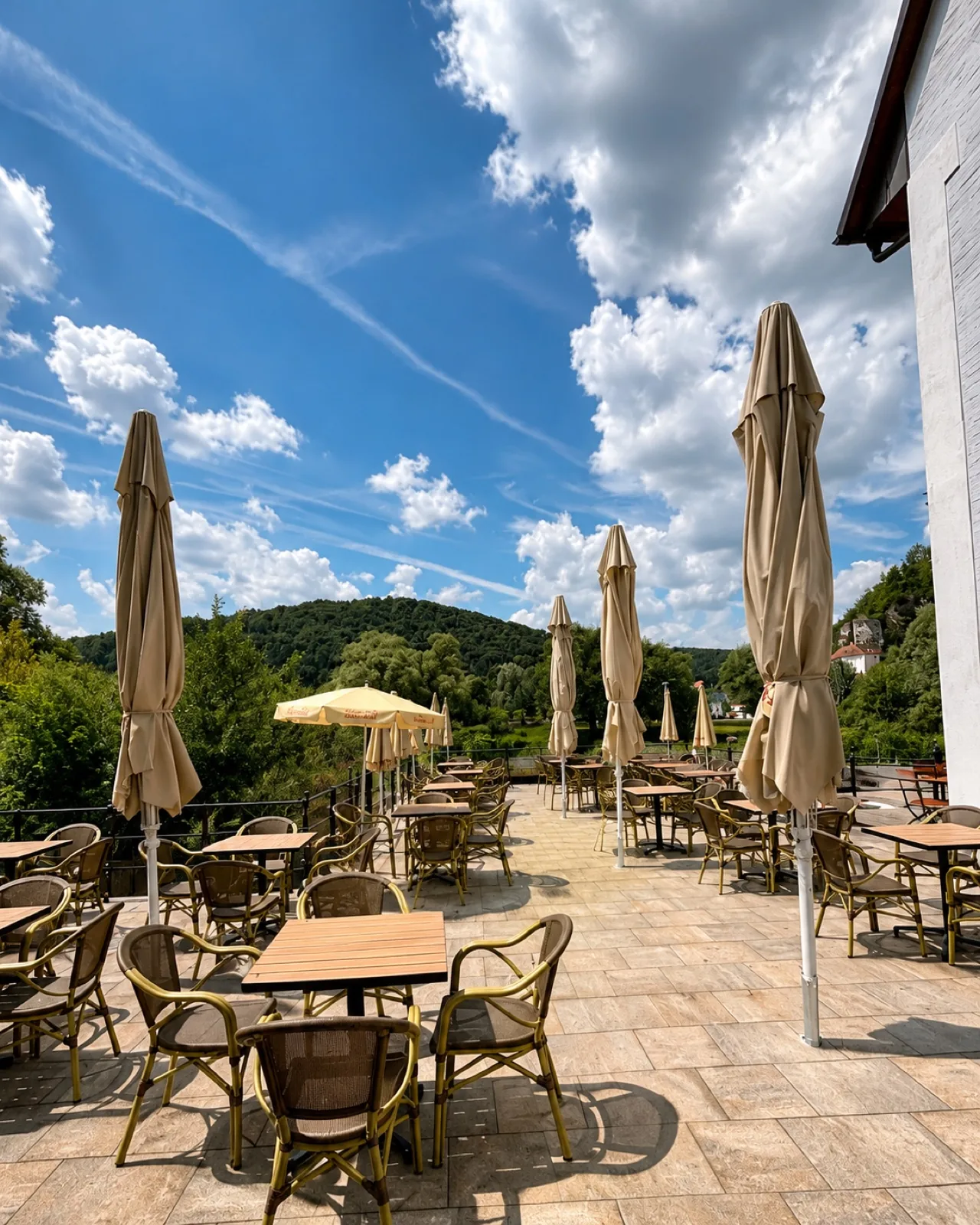 Sonnige Terrasse mit Sonnenschirmen und Korbstühlen, Blick über das grüne Naabtal
